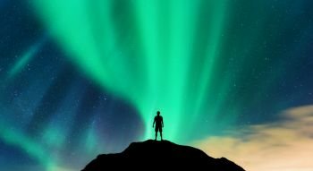 Aurora and silhouette of alone standing man on the mountain peak. Lofoten islands, Norway. Aurora borealis and young man. Sky with stars and green polar lights. Night landscape with northern lights