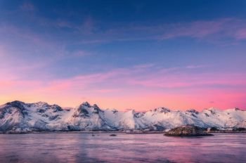 Beautiful snow covered mountains and colorful sky reflected in water at dusk. Winter landscape with sea, snowy rocks, purple sky, reflection, at sunset. Lofoten islands, Norway at twilight. Nature