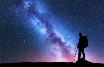 Silhouette of man with backpack and trekking poles against amazing purple Milky Way at night. Space. Landscape with man, bright milky way, sky with stars. Beautiful galaxy. Travel. Starry sky. Nature