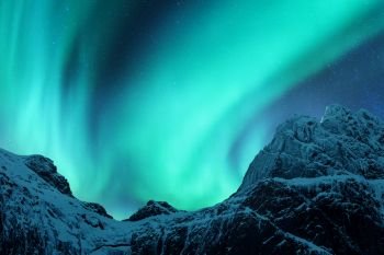 Aurora borealis above the snow covered mountain peak in Lofoten islands, Norway. Northern lights in winter. Night landscape with polar lights, snowy rocks. Starry sky with aurora. Nature background. Aurora borealis above the snow covered mountain peak
