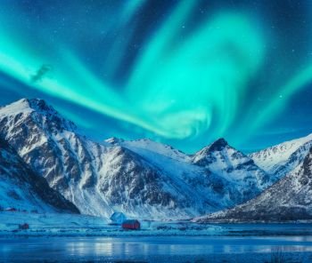 Northern lights above snowy mountains, frozen sea coast and houses in Lofoten islands, Norway. Aurora borealis and small village. Winter landscape with polar lights, rorbu, ice. Aurora over rocks. Northern lights above snowy mountains, frozen sea coast