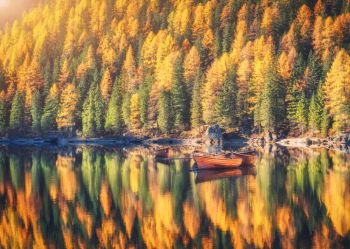 Wooden boats on Braies lake at sunrise in autumn in Dolomites, Italy. Landscape with fall forest, mountains, water with reflection, trees with colorful foliage. Travel in italian alps. Tranquil scene