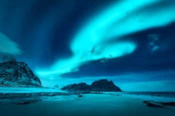 Beautiful aurora borealis. Northern lights in Lofoten islands, Norway. Starry sky with polar lights. Winter landscape with bright aurora, sea, sandy beach and snowy mountains. Uttakleiv beach at night