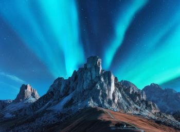 Northern lights above mountains at night in Europe. Aurora borealis. Starry sky with polar lights and high rocks. Beautiful landscape with aurora, road, buildings on the hill, mountain ridge. Travel