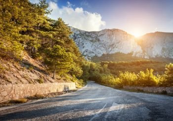 Asphalt country road in mountains with beautiful blue sky in summer at sunset