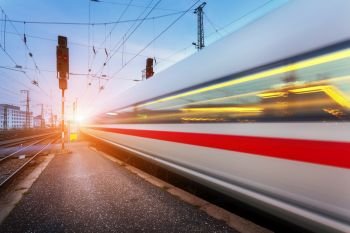 High speed passenger train on railroad track in motion at sunset. Blurred commuter train. Railway station at dusk. Travel background, railway tourism. Industrial landscape. Train