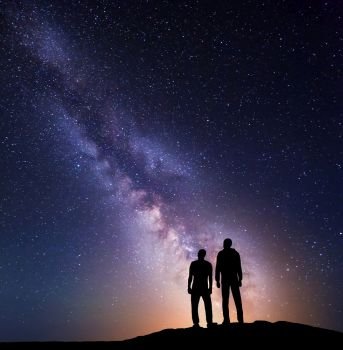Milky Way with silhouette of a family with yellow light on the mountain. Father and a son. Night landscape. Beautiful Universe. Space. Travel background with sky full of stars