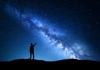 Milky Way. Silhouette of a standing man pointing finger in night starry sky on the mountain. Colorful night landscape with beautiful universe. Travel background with blue sky full of stars and amazing Milky Way