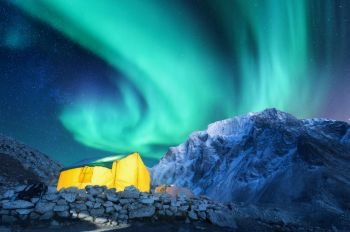 Aurora borealis, yellow glowing tent and snowy mountains. Northern lights, mountain range, starry sky at night in winter. Rocks, sky with stars and polar lights. landscape with green aurora. Space  
