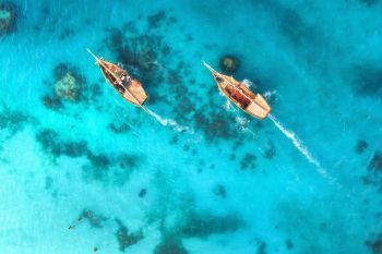 Aerial view of the fishing boats in clear blue water at sunset in summer. Top view from drone of boat, sandy beach. Indian ocean. Travel in Zanzibar, Africa. Landscape with sailboats, sea. Seascape