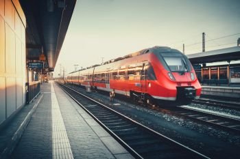 Beautiful railway station with modern red commuter train at colorful sunset in Nuremberg, Germany. Railroad with vintage toning