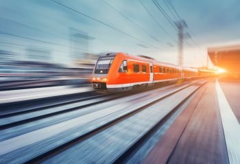 Modern high speed red passenger commuter train in motion at the railway platform at sunset. Railway station. Railroad with motion blur effect. Industrial landscape with train. Vintage toning