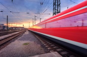 High speed red passenger train on railroad track in motion at sunset. Blurred commuter train. Railway station in Nuremberg, Germany. Industrial landscape