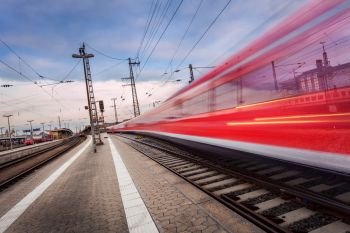 High speed red passenger train on railroad track in motion at sunset. Blurred commuter train. Railway station in Nuremberg, Germany. Industrial landscape