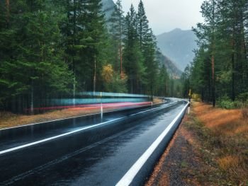 Blurred car on the road in spring forest in rain. Perfect asphalt mountain road in overcast rainy day. Roadway, pine trees in alps. Transportation. Highway in foggy woodland. Car in motion. Travel