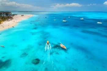 Aerial view of the yachts, fishing boats in clear blue water at sunny day in summer. Top view of boat, sandy beach, palm trees. Travel in Zanzibar, Africa. Colorful landscape with motorboat, sea