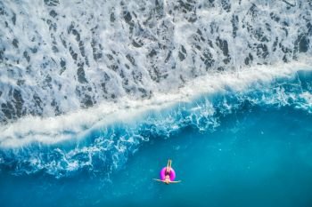 Aerial view of young woman swimming on the pink swim ring in the transparent turquoise sea in Oludeniz,Turkey. Summer seascape with girl, beautiful waves, azure water in sunny day. Top view from drone. Aerial view of young woman swimming on the pink swim ring