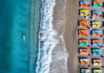 Aerial view of swimming woman in the sea in Oludeniz, Turkey. Summer seascape with girl, clear azure water, waves and sandy beach with colorful chaise-lounges in sunny day. Top view from flying drone . Aerial view of swimming woman in the sea