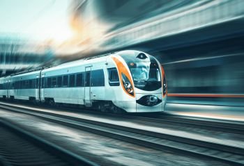 High speed train in motion at the railway station at sunset in Europe. Modern intercity train on the railway platform with motion blur effect. Industrial landscape with passenger train on railroad. High speed train in motion at the railway station
