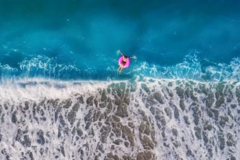 Aerial view of young woman swimming on the pink swim ring in the transparent turquoise sea in Oludeniz,Turkey. Summer seascape with girl, beautiful waves, azure water at sunrise. Top view from drone. Aerial view of young woman swimming on the pink swim ring