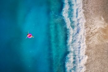 Aerial view of young woman swimming on the pink swim ring in the transparent turquoise sea in Oludeniz,Turkey. Summer seascape with girl, beautiful waves, azure water in sunny day. Top view from drone. Aerial view of young woman swimming on the pink swim ring