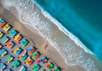 Beautiful young woman on the sea at sunrise in Oludeniz, Turkey. Aerial view of lying woman on the beach with colorful chaise-lounges. Top view from drone. Seascape with girl, azure water and waves. Aerial view of lying woman on the beach