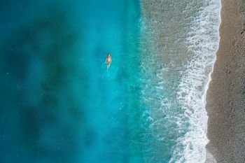 Aerial view of swimming woman in mediterranean sea in Oludeniz, Turkey. Beautiful summer seascape with girl, clear azure water, waves and sandy beach in sunny day. Top view from flying drone. Nature. Aerial view of swimming woman in mediterranean sea