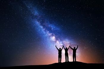 Landscape with colorful Milky Way and silhouette of a happy family with raised-up arms on the mountain. Night starry sky with yellow light. Beautiful Universe. Space background