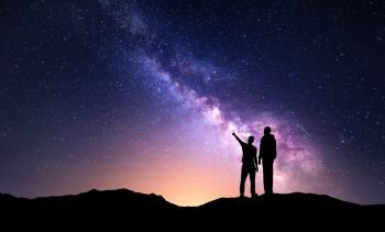 Milky Way with silhouette of a family and yellow city lights. Father and a son who pointing finger in night starry sky on the mountain. Night landscape. Beautiful Universe. Space. Travel background with sky full of stars