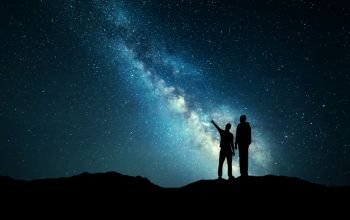Milky Way with silhouette of a family. Father and a son who pointing finger in night starry sky on the mountain. Night landscape. Beautiful Universe. Space. Travel background with sky full of stars