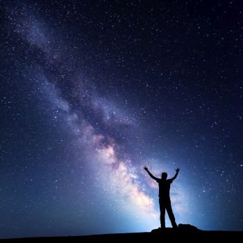 Landscape with colorful Milky Way. Night sky with stars and silhouette of a happy man with raised up arms on the mountain. Beautiful Universe. Space background