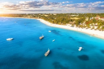 Aerial view of the yachts and boats on tropical sea coast with sandy beach at sunset. Summer holiday in Zanzibar, Africa. Landscape with boat, yacht, clear blue water, green palm trees, sky. Top view
