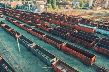 Aerial view of freight trains. Top view of old rusty wagons on railroad. Heavy industry. Industrial landscape with train, green trees and grass at sunset in summer. Railway station. Transportation 