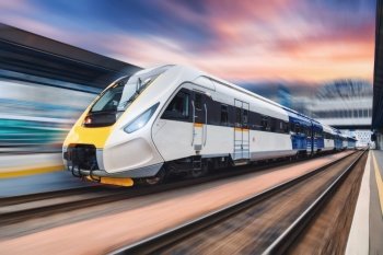 High speed train in motion on the railway station at sunset. Modern intercity passenger train with motion blur effect on the railway platform. Industrial. Railroad transportation in Europe. Industry