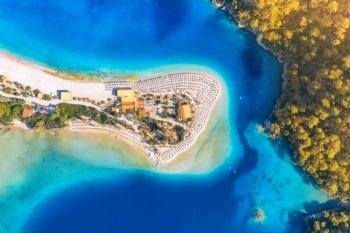 Aerial view of sandy beach with umbrellas, green forest, mountain at sunset in summer. Blue lagoon in Oludeniz, Turkey. Tropical landscape with sea bay, island, white sandy bank, blue water. Top view