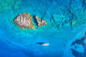 Aerial view of beautiful yacht on the sea and rocks at sunset in summer in Turkey. Top view of boat, stones, clear blue water. Tropical landscape. Travel. Nature background. View from above. Cruise