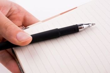 Hand holding a notebook with a pen on a white background