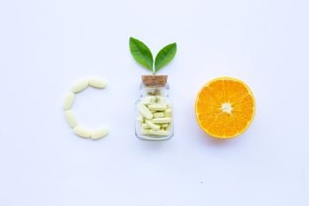 Vitamin C bottle and pills with orange fruit on white background.