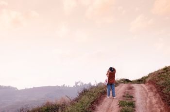 FEB 3, 2018 Chiang Mai, Thailand : Young woman taking photo of sunset sky on dirt path country road on the hill at evening in Chiang Mai