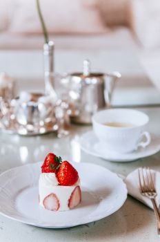 Creamy rich Strawberry shortcake on white dish at tea time with tea set