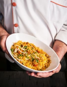 Male chef holding Chicken briyani rice bowl with both hands, close up shot