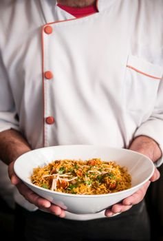 Male chef holding Chicken briyani rice bowl with both hands, close up shot