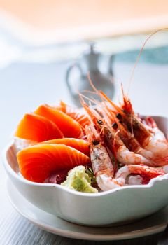 Fresh Japanese sashimi, raw salmon, sweet Ebi shrimps and wasabi in white bowl. Close up shot