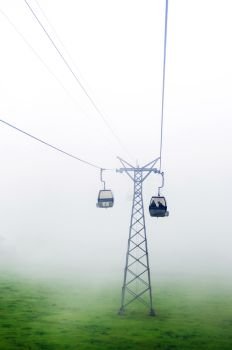SEP 29, 2013 Engelberg, Switzerland - Ropeway Gondola flying over green grass field of foot of mount Titlis alpine mountain valley on foggy day.
