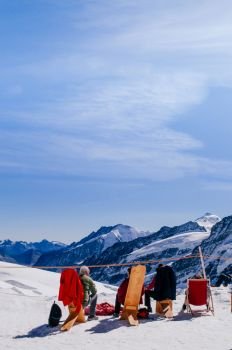 SEP 24, 2013 Jungfraujoch, Switzerland - Tourists sit on wooden chair in winter snow landscape on Jungfraujoch, top of Europe Swiss alps scenery.