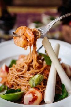 Close up shot of Fusion spaghetti shrimp pasta with Thai Tom Yum Gung spicy sauce, kaffir lime leaves, lemongrass and tomatoes