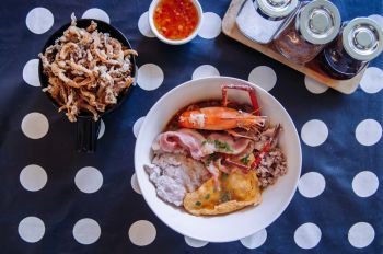 Thai seafood noodle with pork, bacon, river prawn, crispy fried mushroom and condiments set on polka dot tablecloth