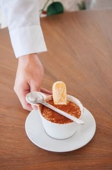 Waiter hand serving Italian Tiramisu in white cup with ladyfinger biscuit or Savoiardi