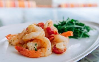 Stirfried shrimps with butter garlic lemon sauce, fresh tomatoes and Arugula rocket salad in white plate. close up shot