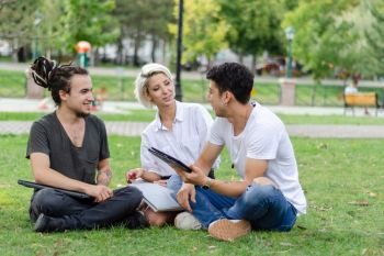 Young woman and two young men are working in the park with a laptop.They look at each other, smiling.